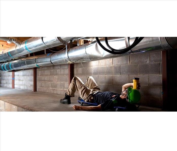 man laying with protective helmet laying on back looking up with a flashlight at air ducts