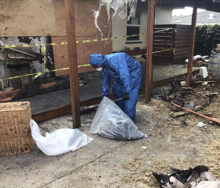 technician in blue ppe suit picking up fire damaged yard debris
