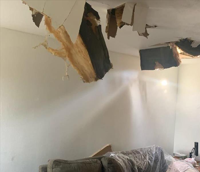 drywall opened in ceiling with insulation hanging and on the couch below